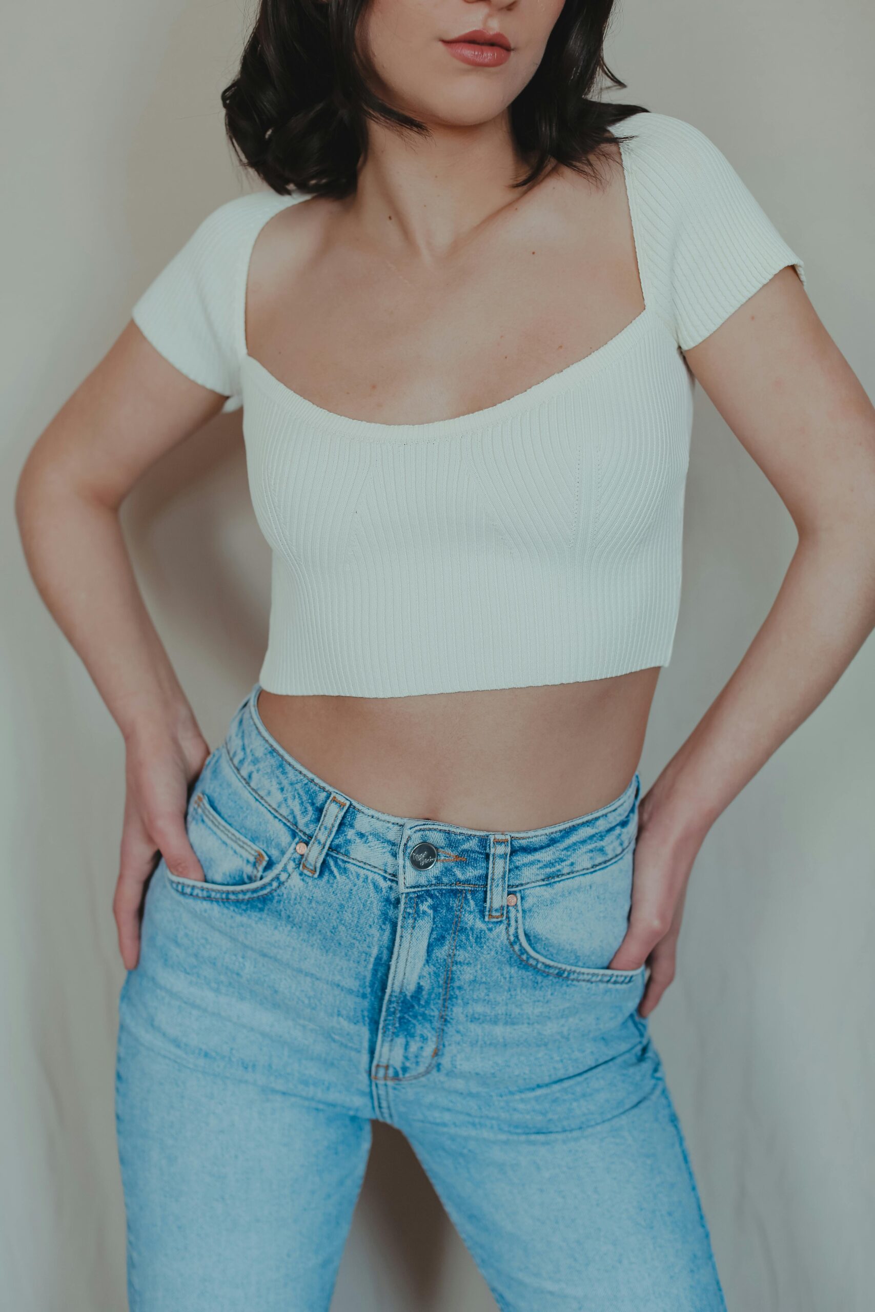 Stylish woman posing in a white crop top and denim jeans indoors.